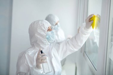 Koruyucu giysiler ve tıbbi maskeler giyen sağlık görevlileri pencere camlarını temizleyip dezenfekte ediyorlar.