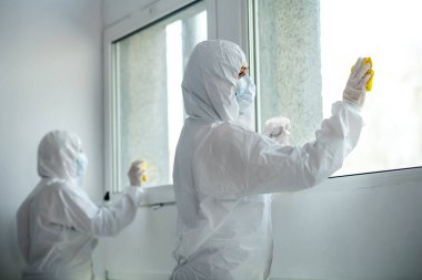 Koruyucu giysiler ve tıbbi maskeler giyen sağlık çalışanları pencereyi dezenfekte ediyor.