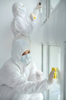 Koruyucu giysiler ve tıbbi maskeler giyen sağlık çalışanları pencereyi dezenfekte ediyor.