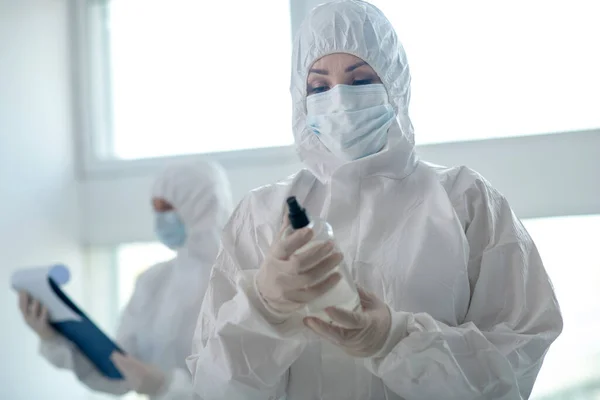 Жінка-медик у захисному одязі та медичній масці, що тримає антисептик — стокове фото