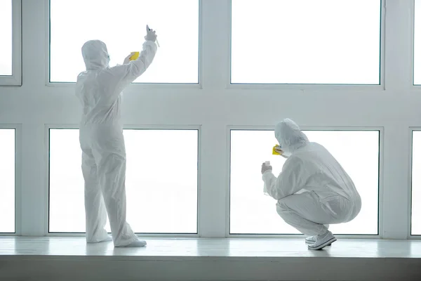 Medical workers in protective clothing and medical masks cleaning and disinfecting window panes