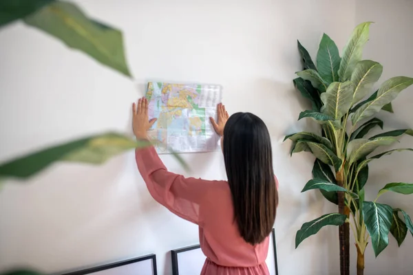 Mulher de cabelos escuros segurando mapa do mundo contra a parede, estudando-o — Fotografia de Stock