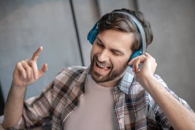 Koyu saçlı, sakallı, kulaklıklı bir adam şarkı söylüyor.