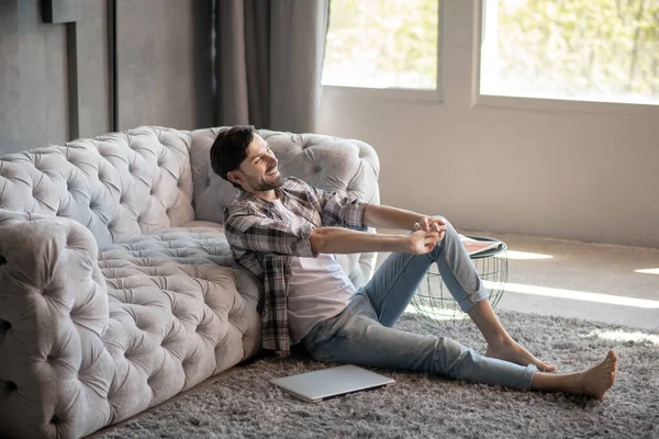 Hombre sentado en el suelo cerca del sofá descansando . — Foto de Stock