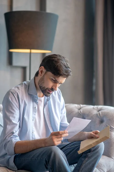 Un hombre serio con una carta en las manos sentado en el sofá . — Foto de Stock