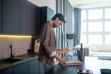 Genç sakallı adam elinde bir zarf tutuyor ve konsantre görünüyor.