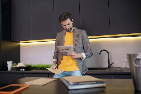 Joven barbudo leyendo un periódico y sonriendo — Foto de Stock