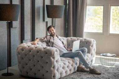 Kanepede rahat bir odada dizüstü bilgisayarı olan bir adam.