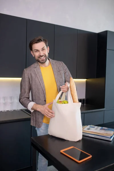 Молодий бородатий чоловік тримає сумку з їжею і виглядає весело — стокове фото
