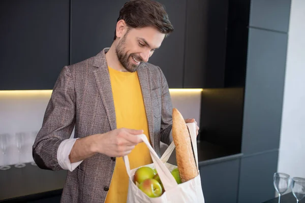 Молодий бородатий чоловік відкриває сумку з їжею і посміхається — стокове фото