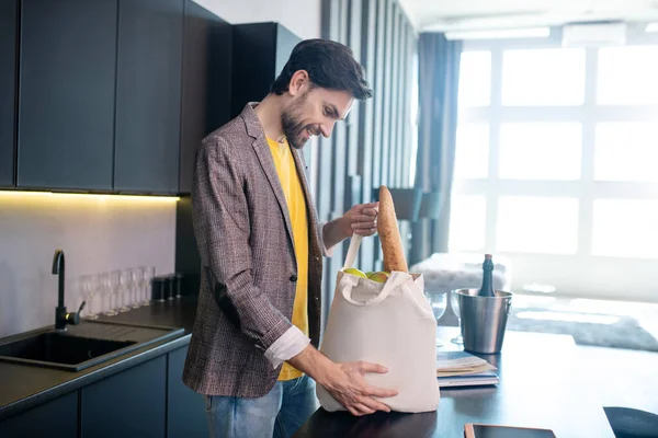 Joven barbudo tomando la baguette de pan de la bolsa — Foto de Stock