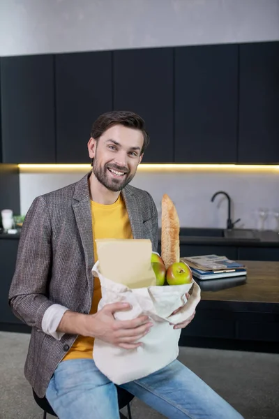 Joven barbudo sosteniendo una bolsa con comida y sonriendo — Foto de Stock