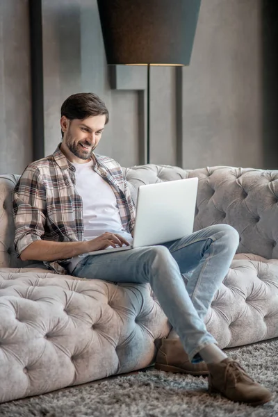 Dark-haired bearded man on the couch with a laptop. — Stock Photo, Image