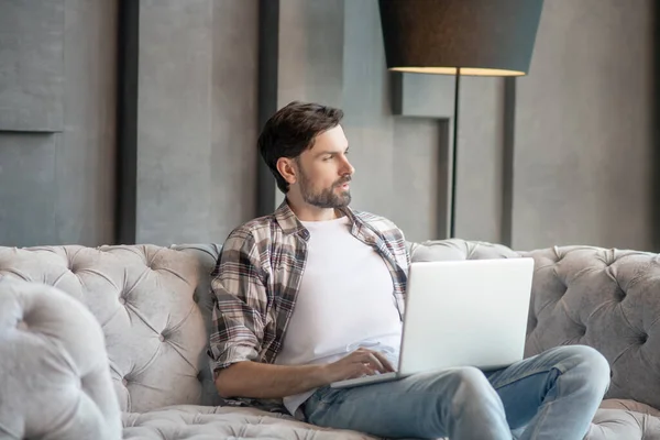 Pensive man in a plaid shirt with a laptop. — Stock Photo, Image