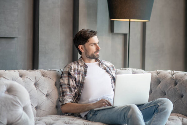 Pensive man in a plaid shirt with a laptop.