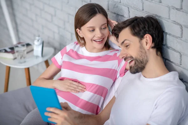 Donna incinta e suo marito navigare su internet e guardare rilassato — Foto Stock