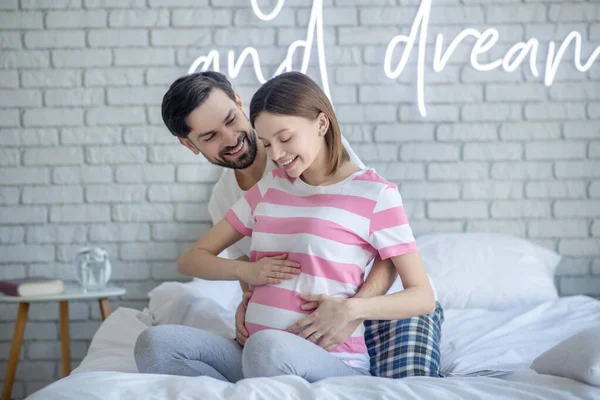 Homem de cabelos escuros abraçando sua linda esposa grávida — Fotografia de Stock