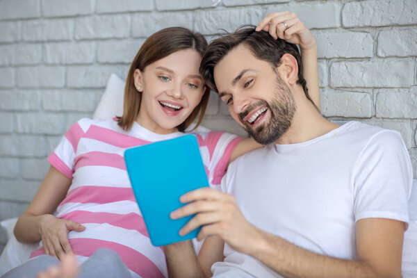 Pregnant woman and her husband surfing internet and feeling happy