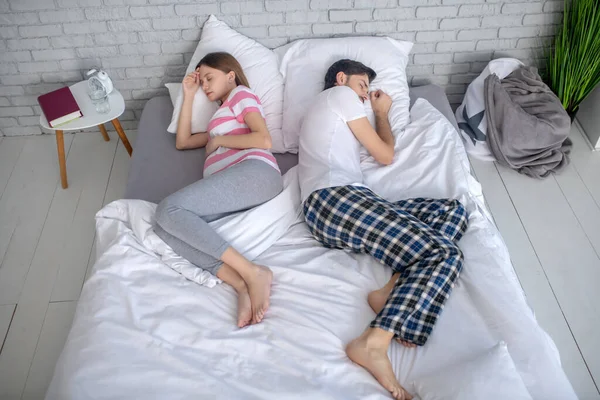 Беременная молодая женщина в полосатой футболке и ее муж спит на большой кровати — стоковое фото
