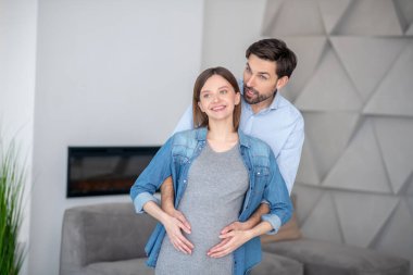 Genç siyah saçlı, hamile karısına sarılıyor.