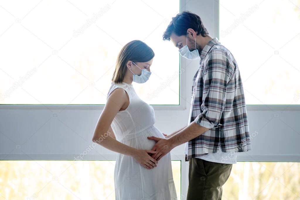 Tall man in a mask touching pregnant abdomen of his wife