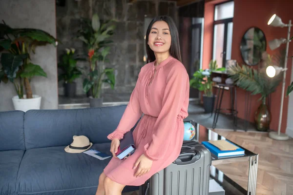 Mulher de cabelos escuros feliz sentada na mala, esperando por sua jornada, sorrindo — Fotografia de Stock