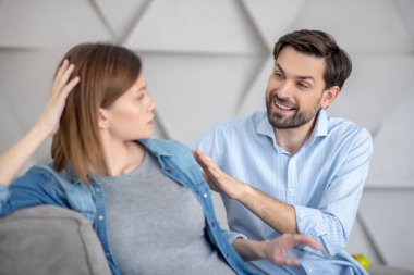 Genç sakallı adam karısının omzuna dokunuyor ve gülümsüyor.