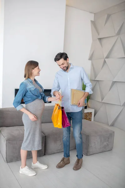 Koyu saçlı adam hamile karısına alışveriş torbaları veriyor. — Stok fotoğraf