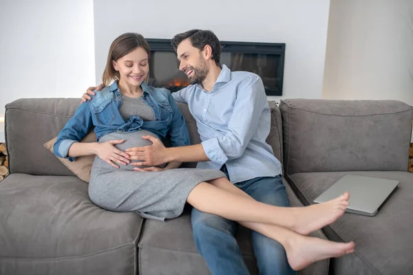청바지를 입은 젊은 임신부 가집에서 남편 과 함께 있으면 기분 이 좋아 진다 — 스톡 사진