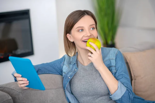 Молодая беременная женщина в джинсовой куртке ест яблоко — стоковое фото