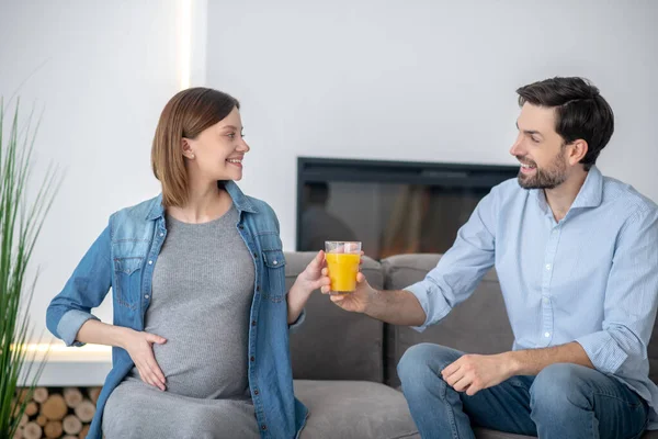 Gondoskodó férj ad egy pohár narancslevet terhes feleségének és mosolyog. — Stock Fotó