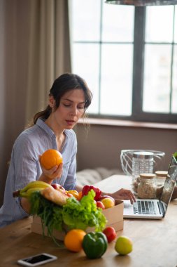 Gri elbiseli kız masada oturuyor ve elinde bir portakal tutuyor.