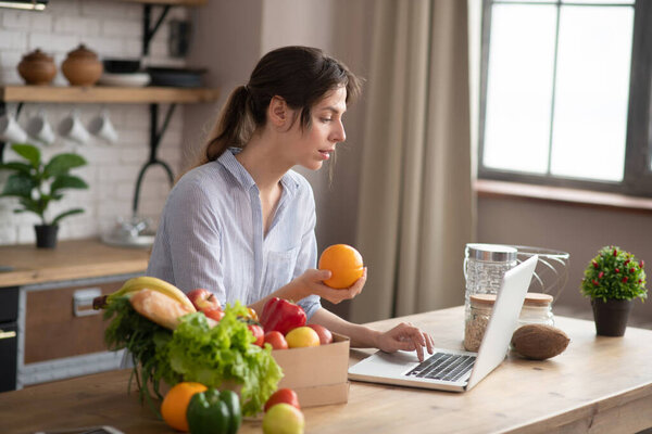 Girl in grey homewear sitting at the table and holding an orange