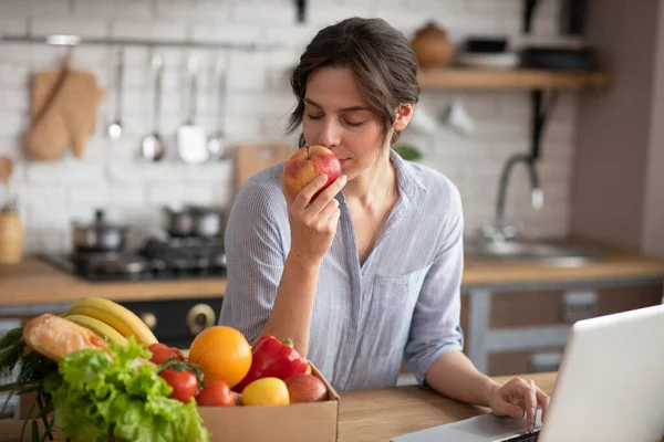 Chica en ropa de casa gris sentada a la mesa y oliendo una manzana — Foto de Stock