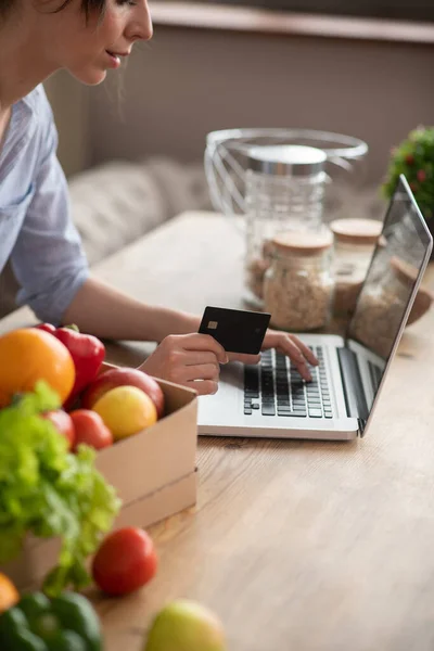 Girl in grey homewear sitting at the laptop and paying by card — Stock Photo, Image