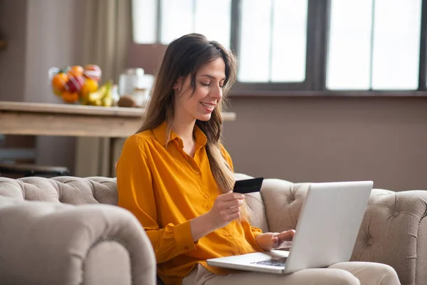 Lang haar meisje in een mosterd kleur blouse betalen op internet en zich comfortabel voelen — Stockfoto