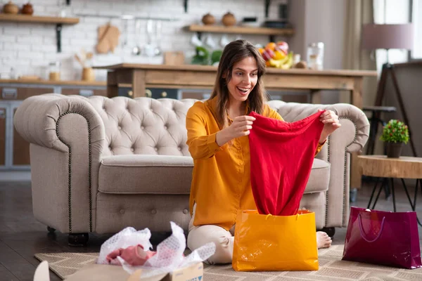 Chica de pelo largo en una blusa de color mostaza sosteniendo un nuevo vestido y sintiéndose feliz — Foto de Stock