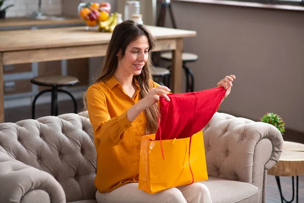 Chica de pelo largo en una blusa de color mostaza sosteniendo ropa nueva y sintiéndose emocionada — Foto de Stock