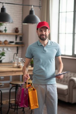 Kırmızı şapkalı teslimatçı elinde kutular ve alışveriş torbaları tutuyordu.