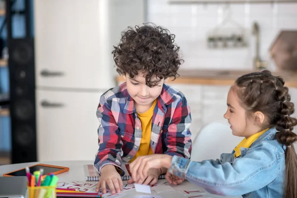 Lockiger Junge und dunkelhaariges Mädchen sitzen am runden Tisch, spielen mit Buchstaben des Alphabets, haben Spaß — Stockfoto