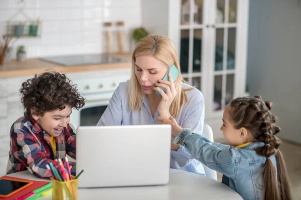 Blonde female working on laptop and talking on mobile, girl grabbing woman hand — Stock Photo, Image