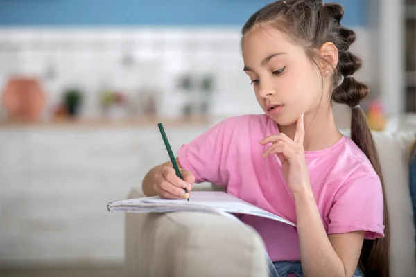 Chica morena involucrada sentada en el sofá, escribiendo en su cuaderno —  Fotos de Stock