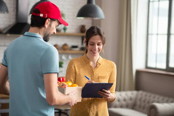 Cliente donna dai capelli scuri firma la lettera di vettura dopo aver ricevuto la spesa e sorridente — Foto Stock