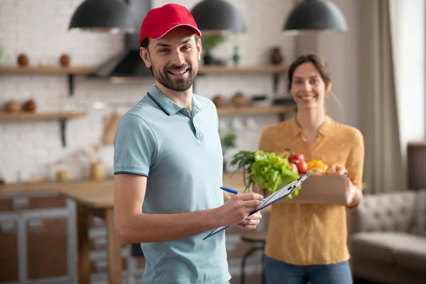 Cortesano joven en un sombrero rojo sosteniendo comestibles y sonriendo — Foto de Stock