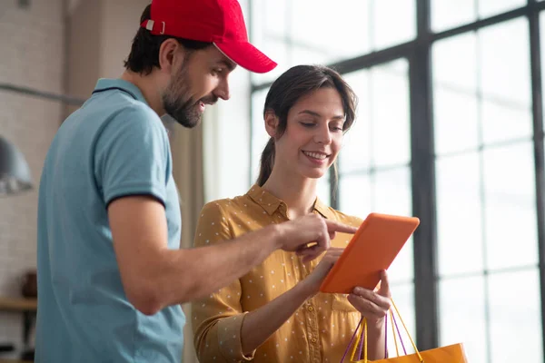 Entregue uma pessoa com um chapéu vermelho mostrando algo em um tablet para uma cliente feminina — Fotografia de Stock