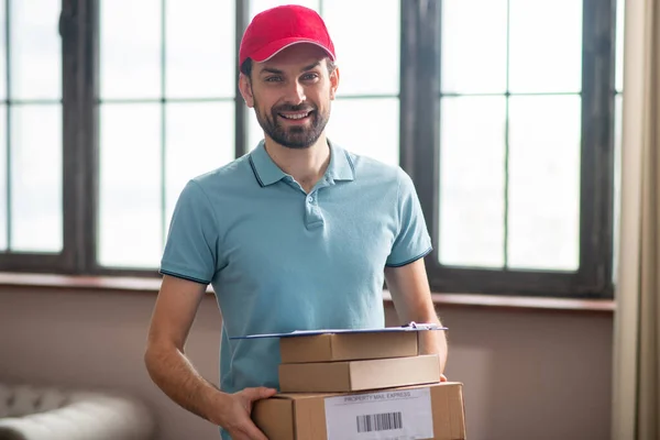 Entrega persona de pie en la cocina y sosteniendo las cajas en sus manos y sonriendo — Foto de Stock