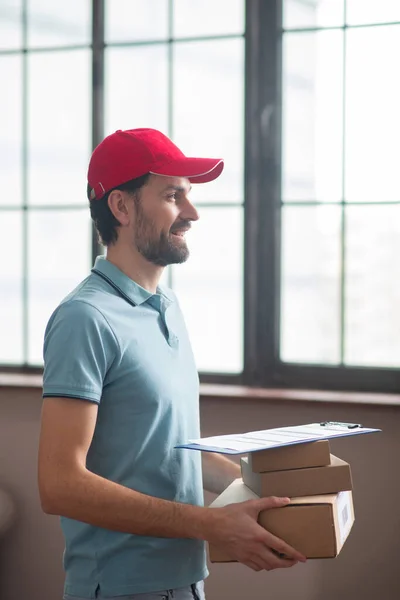 Delivery person standing in the kitchen and holding the boxes in his hands and looking positive