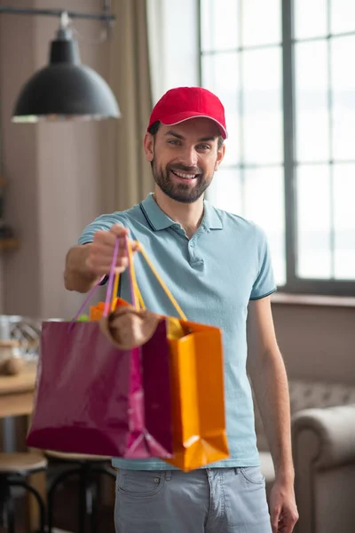 Delivery person in a red hat holding shopping bags