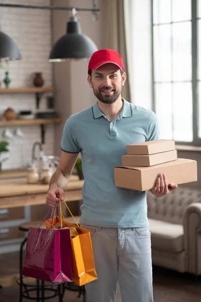 Entrega persona en un sombrero rojo sosteniendo las cajas y bolsas de la compra — Foto de Stock
