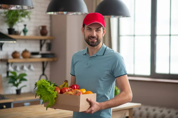 Чоловік у червоному капелюсі тримає коробку з продуктами на столі — стокове фото